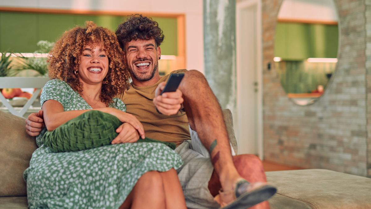 A couple laughing and watching TV  whose data will be collected via ERS's tv field and survey research solution.